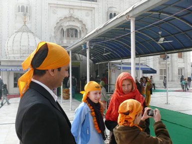 Eine Gruppe von Menschen mit orangen Turbanen steht vor einem beeindruckenden Gebäude in Neu-Delhi und lächelt.