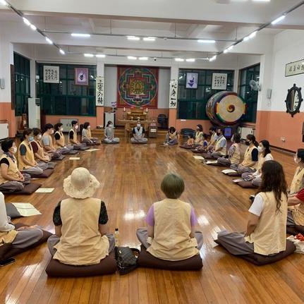 Eine Gruppe von Menschen sitzt in einem Meditationsraum, umgeben von traditionellen Kunstwerken und einem großen Gong.