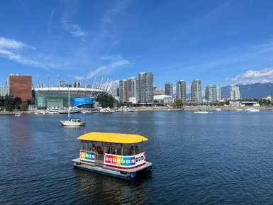 Ein buntes Aquabus-Boot fährt auf dem ruhigen Wasser vor der beeindruckenden Skyline von Vancouver.