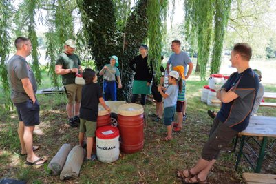 Eine Gruppe von Erwachsenen und Kindern versammelt sich unter einem Baum, um Ausrüstung für eine Kanutour vorzubereiten.