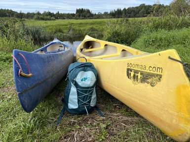 Zwei Kanus, eines blau und das andere gelb, stehen am Ufer eines ruhigen Gewässers, umgeben von üppigem Grün.