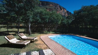 Zwei Liegen mit Leopardenmuster stehen neben einem glitzernden Pool, umgeben von üppigem Grün und majestätischen Bergen.