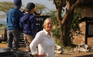 Eine Frau lächelt vor einem Schild, während zwei Kinder auf einem Geländewagen stehen und die Umgebung erkunden.