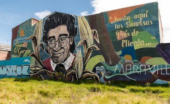 Ein großes Wandgemälde zeigt ein Porträt eines lächelnden Mannes mit Brille, umgeben von bunten Pflanzenmotiven.