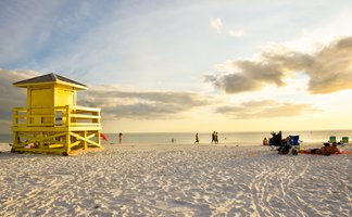 Ein leuchtend gelbes Rettungshaus steht am Strand, während Menschen im warmen Sonnenlicht spazieren gehen.