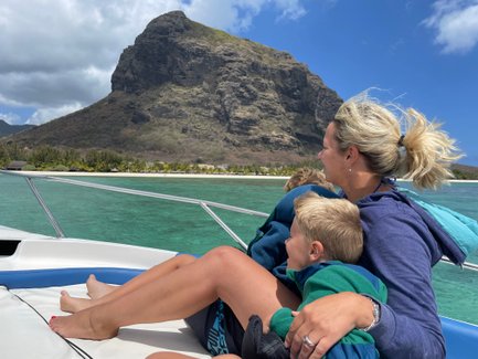 Eine Mutter sitzt auf einem Boot und umarmt ihre beiden Kinder, während sie die Aussicht auf die grüne Lagune genießen.