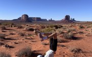 Ein Kind macht einen Handstand auf dem roten Sandboden, umgeben von beeindruckenden Felsformationen unter klarem Himmel.