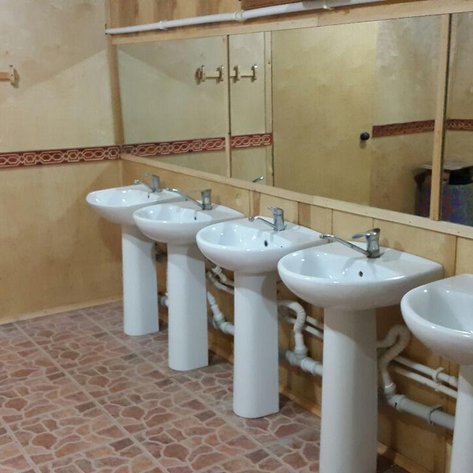 Ein sauberer, gut beleuchteter Waschraum mit fünf weißen Waschbecken und einem großen Spiegel an der Wand.