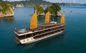 Ein elegantes Kreuzfahrtschiff mit gelben Segeln gleitet über das ruhige Wasser der Lan Ha Bucht, umgeben von grünen Felsen.