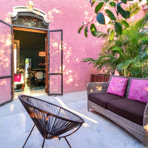 Eine einladende Terrasse mit einem gemütlichen Sofa und einem Stuhl, umgeben von üppigem Grün und einer pinken Wand.