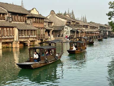 Drei traditionelle Holzboote gleiten sanft auf dem klaren Wasser, umgeben von historischen Gebäuden in Wuzhen.