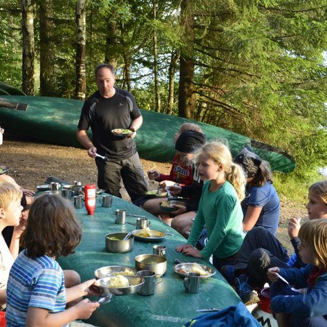 Eine Gruppe von Kindern sitzt an einem Tisch im Freien und genießt eine Mahlzeit inmitten der Natur.