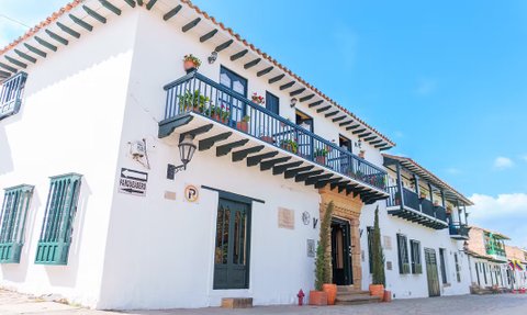 Ein charmantes, weißes Gebäude mit einem blauen Balkon, geschmückt mit blühenden Pflanzen und einer einladenden Eingangstür.