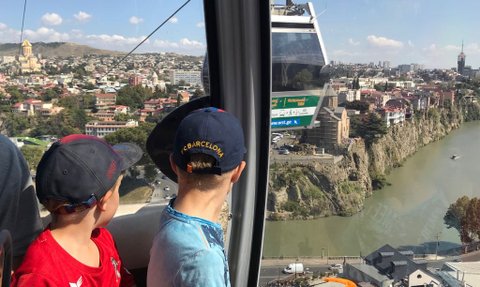 Zwei Kinder in einer Seilbahn blicken auf die Stadt und den Fluss, während sie die Aussicht genießen und spielen.