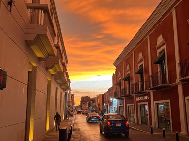 Eine belebte Straße in Valladolid, beleuchtet von einem beeindruckenden orangefarbenen Sonnenuntergang am Abend.