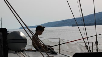 Ein Junge sitzt auf einem Segelboot und hält eine Angelrute, während er nachdenklich auf das Wasser blickt.