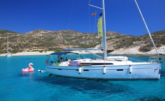 Ein Segelboot schaukelt sanft auf dem klaren, blauen Wasser, während ein pinker Flamingo-Schwimmring daneben schwimmt.