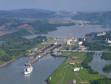 Ein Schiff fährt durch den Panamakanal, umgeben von üppigem Grün und einer beeindruckenden Landschaft im Hintergrund.