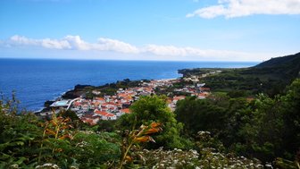 Ein malerischer Blick auf ein Küstendorf mit roten Dächern, umgeben von üppigem Grün und dem blauen Ozean im Hintergrund.