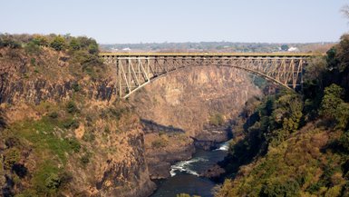Eine beeindruckende Eisenbahnbrücke überspannt eine tiefe Schlucht, umgeben von üppigem Grün und steilen Felsen.
