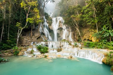 Majestätische Wasserfälle stürzen über Felsen, umgeben von üppigem Grün und sanftem, türkisfarbenem Wasser.