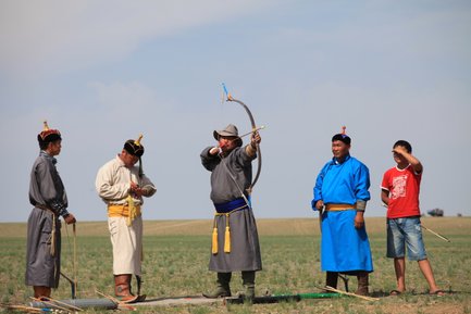 Eine Gruppe von Männern in traditioneller Kleidung, die beim Bogenschießen auf einer weiten, grünen Wiese stehen.