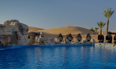 Ein glitzernder Pool in einer Wüstenlandschaft, umgeben von Palmen und stilvollen Liegen für entspannende Momente.