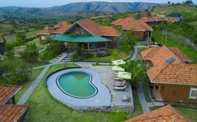 Eine Luftaufnahme des Kigarama Lodges zeigt ein Schwimmbad in Herzform, umgeben von grünen Wiesen und rustikalen Hütten.