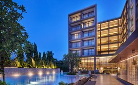 Ein elegantes Hotelgebäude mit beleuchteten Balkonen, umgeben von üppigem Grün und einem glitzernden Pool bei Dämmerung.