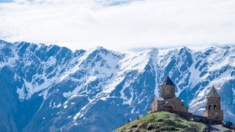 Die majestätische Gergeti Kirche thront auf einem Hügel, umgeben von schneebedeckten Bergen und strahlend blauem Himmel.