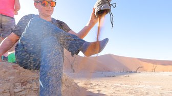 Ein Kind leert seinen Schuh aus, in dem sich Sand befindet - Namibia Rundreise mit Kindern