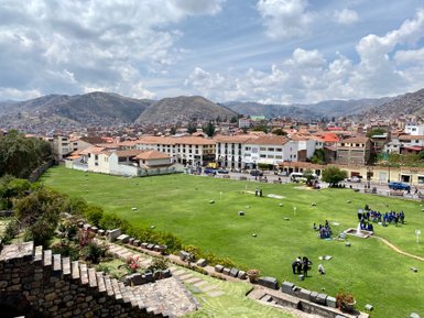 Eine weite Aussicht auf Cusco mit grünen Wiesen, historischen Gebäuden und den majestätischen Anden im Hintergrund.