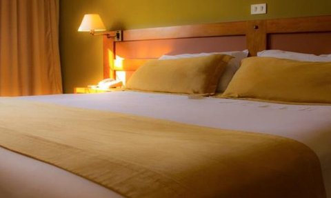 Ein gemütliches Hotelzimmer mit einem großen Bett, gelben Kissen und sanfter Beleuchtung, die eine entspannende Atmosphäre schafft.