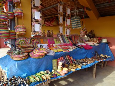Bunte handgefertigte Körbe und Kunsthandwerk sind auf einem blauen Tuch in einem Marktstand ausgestellt.