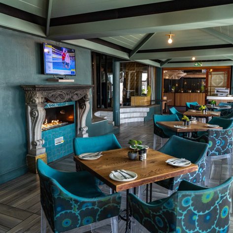 Ein elegantes Restaurant mit blauen Stühlen und Holztischen, das eine gemütliche Atmosphäre mit einem Kamin bietet.