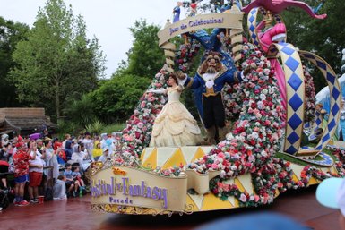 Eine festliche Parade im Magic Kingdom zeigt Belle und das Biest, umgeben von bunten Blumen und fröhlichen Zuschauern.
