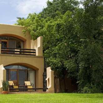 Eine malerische Lodge mit großen Fenstern und einem Balkon, umgeben von üppigem Grün und einem gepflegten Rasen.