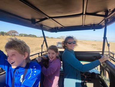 Zwei Kinder und eine Frau genießen eine Jeep-Safari, während sie fröhlich in die Landschaft blicken.