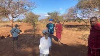 Eine Gruppe von Menschen, darunter Kinder und Maasai, erkundet die trockene Landschaft des Amboseli-Nationalparks.