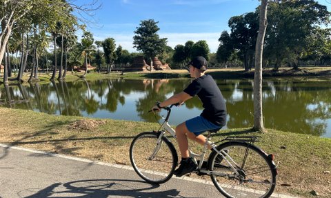 Junge fährt mit Fahrrad durch die Anlage von Wat Mahathat in Sukhothai - Thailand Familienreise