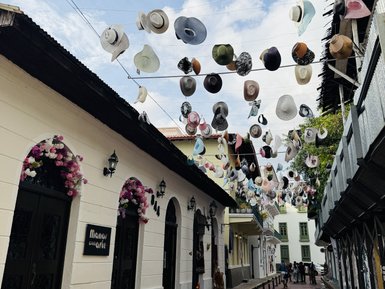 Bunte Hüte hängen über einer lebhaften Straße in der Altstadt, umgeben von charmanten, historischen Gebäuden.