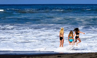 Drei Mädchen stehen am Strand, während die Wellen sanft an den Ufer schlagen und sie fröhlich miteinander spielen.