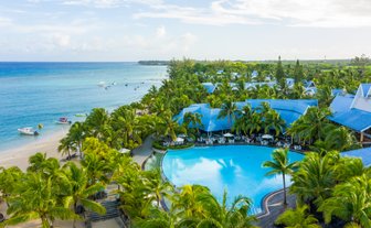 Ein tropisches Resort mit einem großen Pool umgeben von Palmen, Blick auf den klaren Ozean und den farbenfrohen Strand.