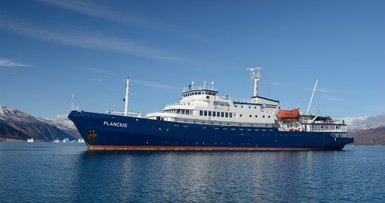 Das Forschungsschiff Plancius liegt ruhig im Wasser, umgeben von majestätischen Bergen und Eisbergen im Hintergrund.