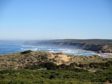 Eine weite Küstenlandschaft mit sanften Wellen, die an den Strand rollen, unter einem klaren blauen Himmel.