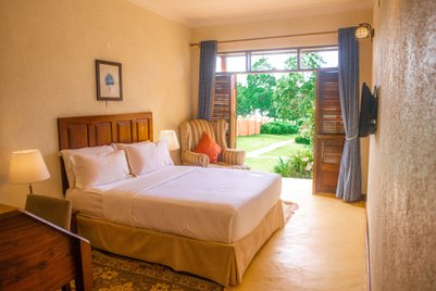 Ein helles Zimmer mit einem großen Bett, einem gemütlichen Sessel und Blick auf den Garten durch offene Fenster.