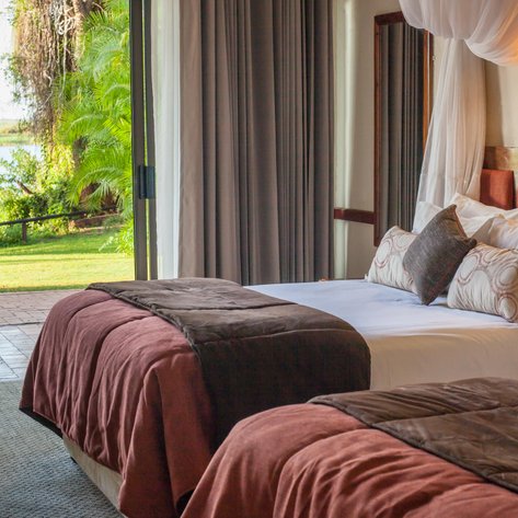 Ein elegantes Zimmer mit zwei Betten, dekoriert mit Kissen, bietet einen Blick auf die grüne Landschaft und den Wasserlauf draußen.