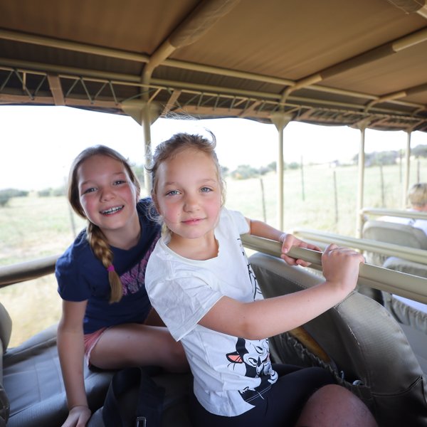 Zwei Mädchen sitzen in einem offenen Safari-Jeep und blicken in die Kamera - Namibia Urlaub mit Kindern