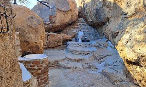 Eine rustikale Außendusche und Toilette, umgeben von großen Felsen und einer natürlichen Steinmauer, schaffen eine einzigartige Atmosphäre.