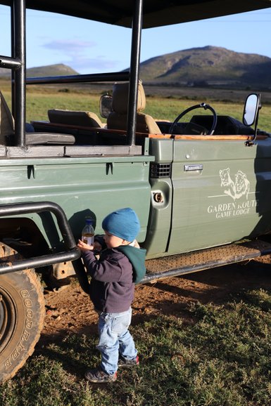 Kleines Kind steht neugierig neben einem Safari-Jeep in der Garden Route Game Lodge – Garden Route Reise mit Kindern
